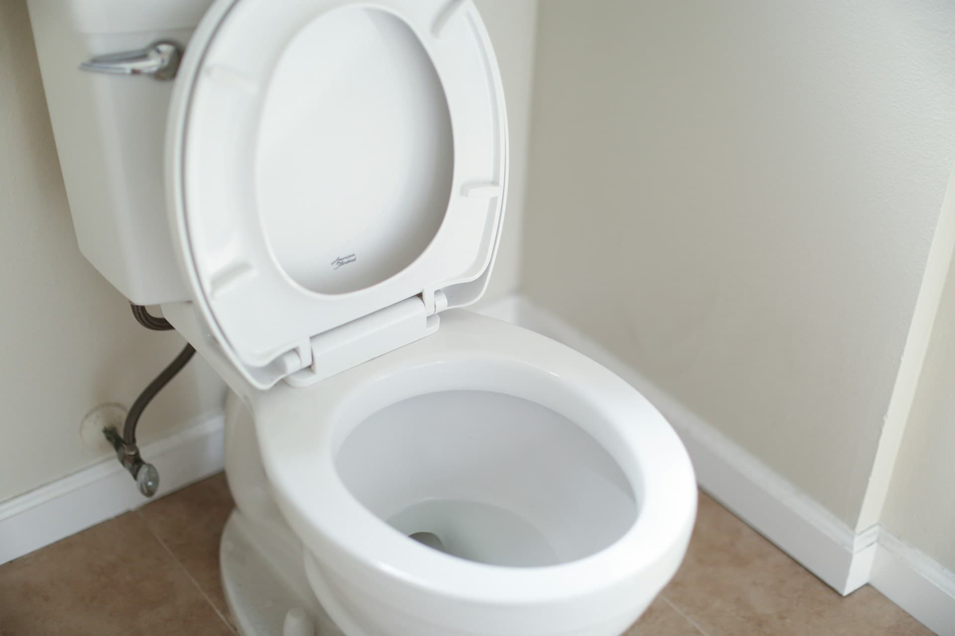 Open white toilet pan and cistern with exposed supply line on tiled floor