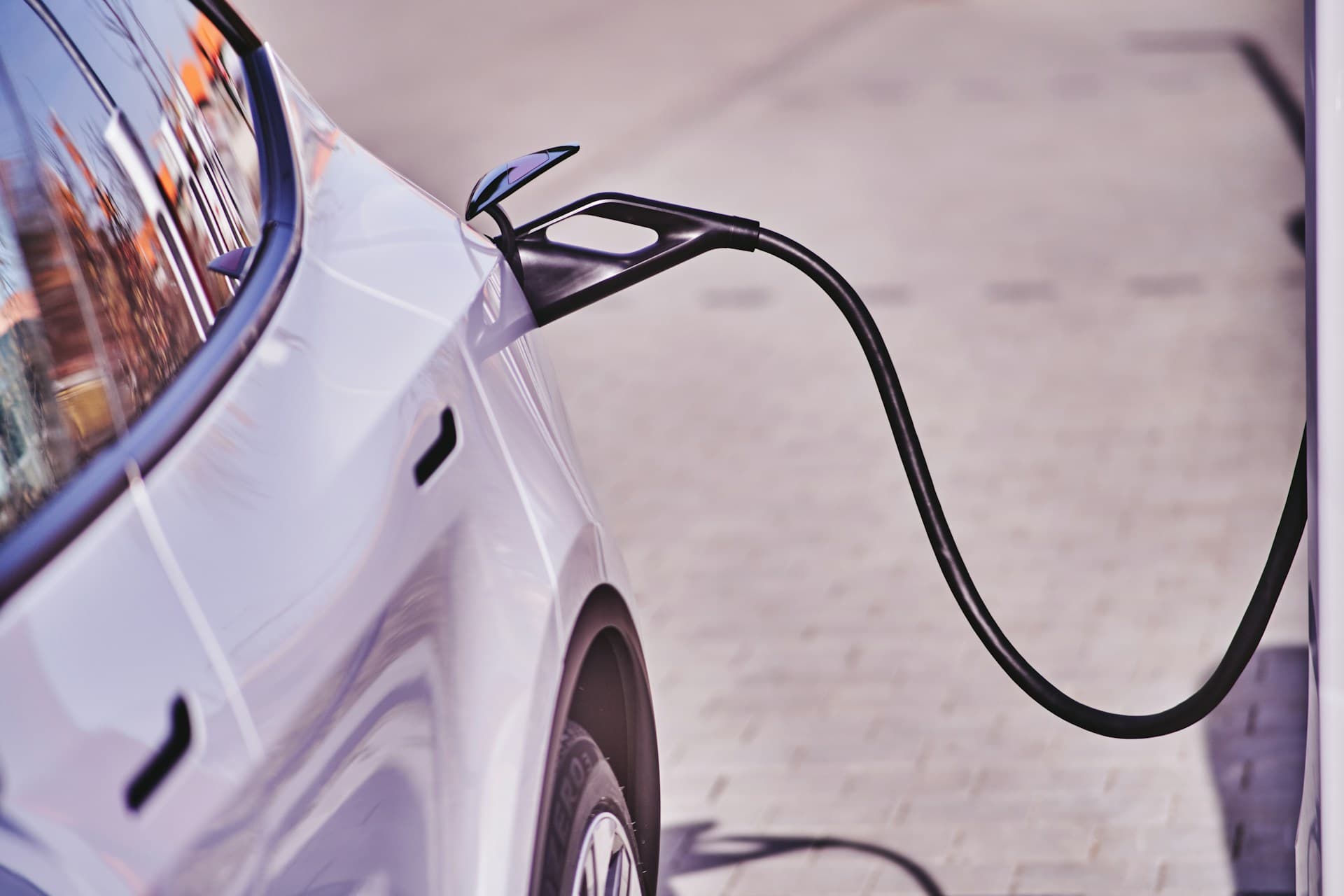 Black charging connector plugged into the charge port of a white electric car