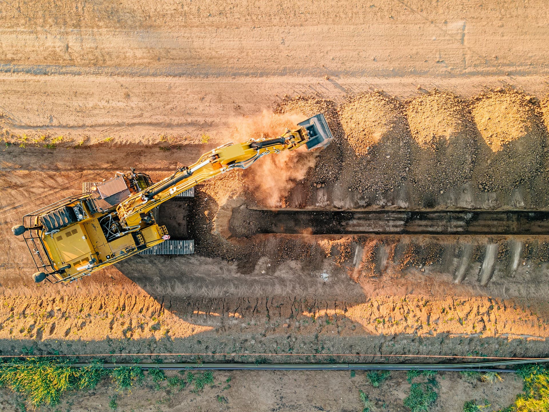 Aerial view of a yellow excavator digging a long trench through dirt