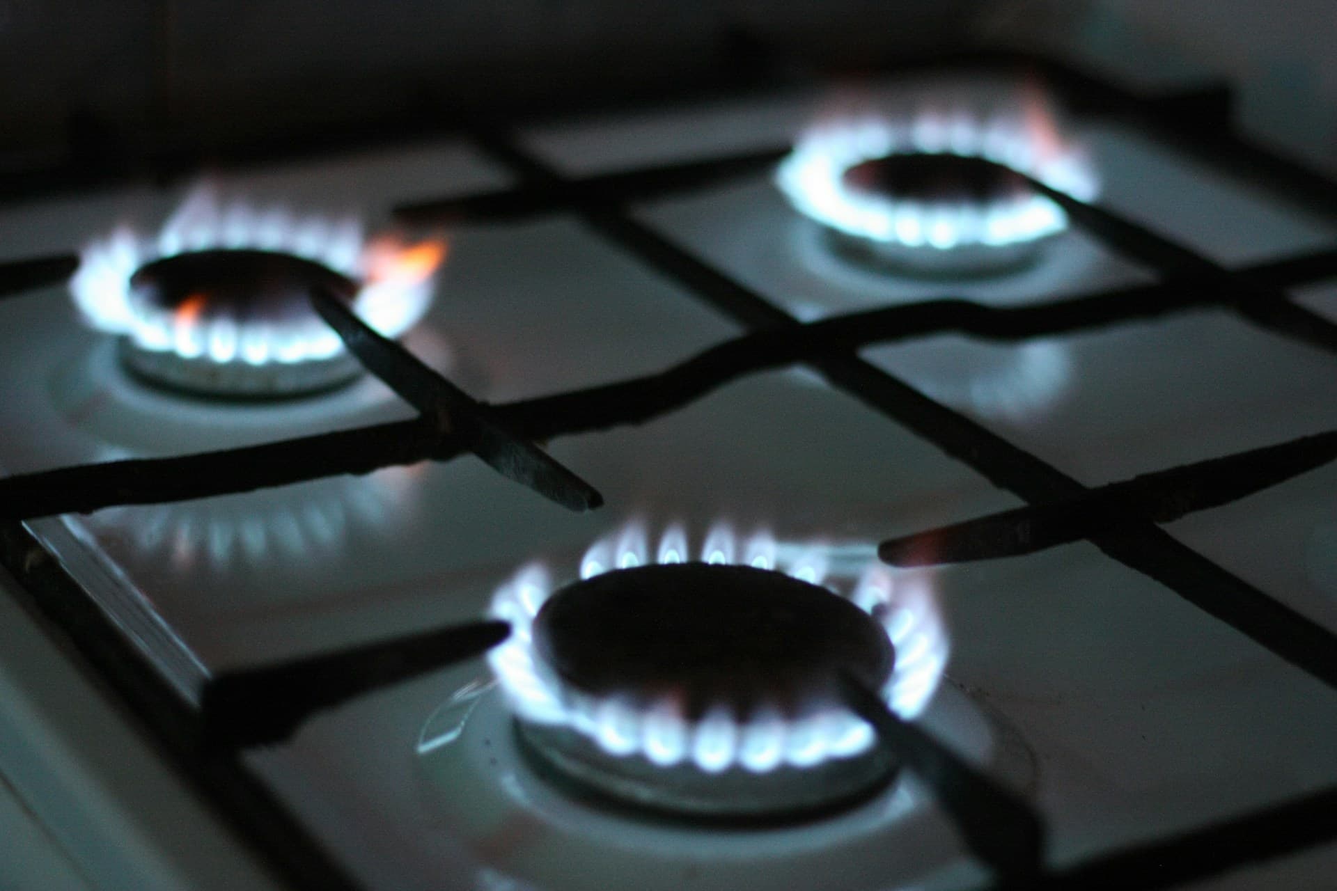 Three lit gas stove burners with blue flames on a white cooktop