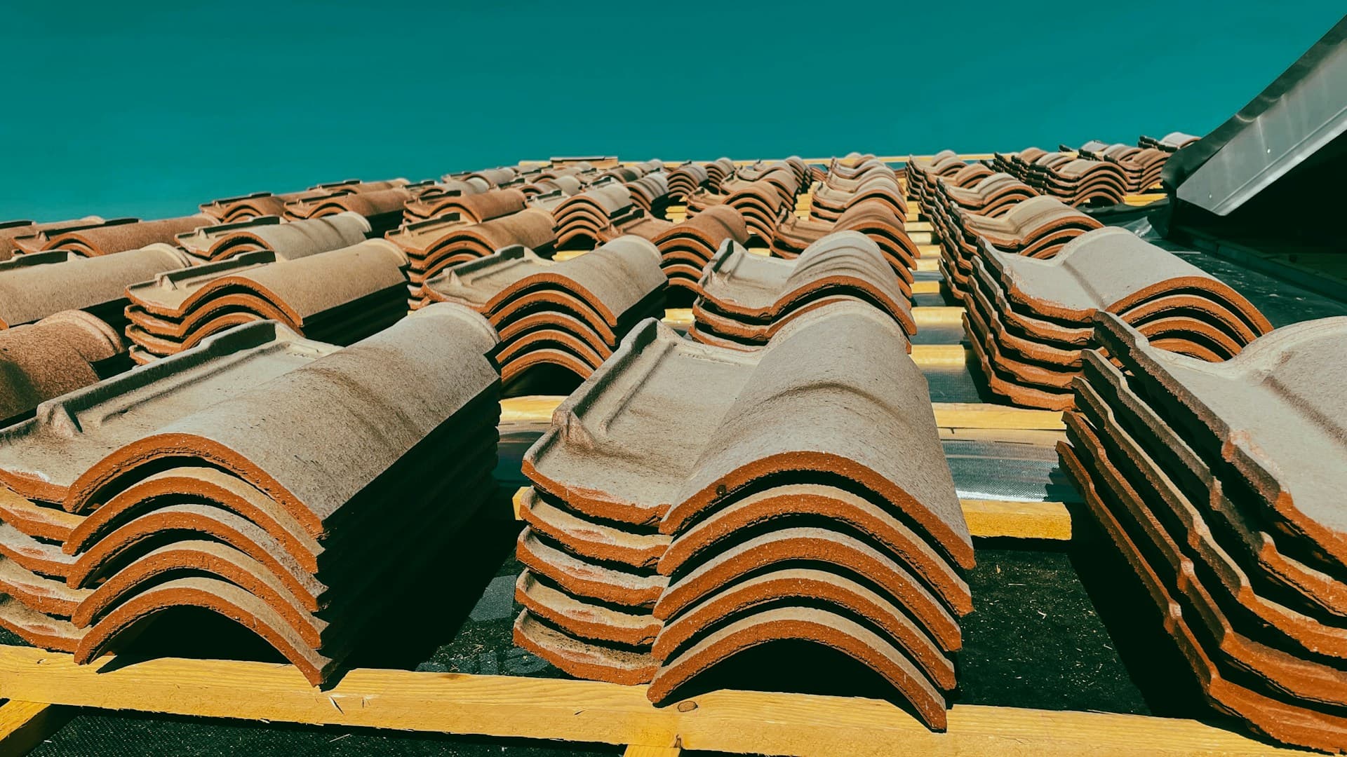 Stacks of curved terracotta roof tiles laid out on roof battens under blue sky