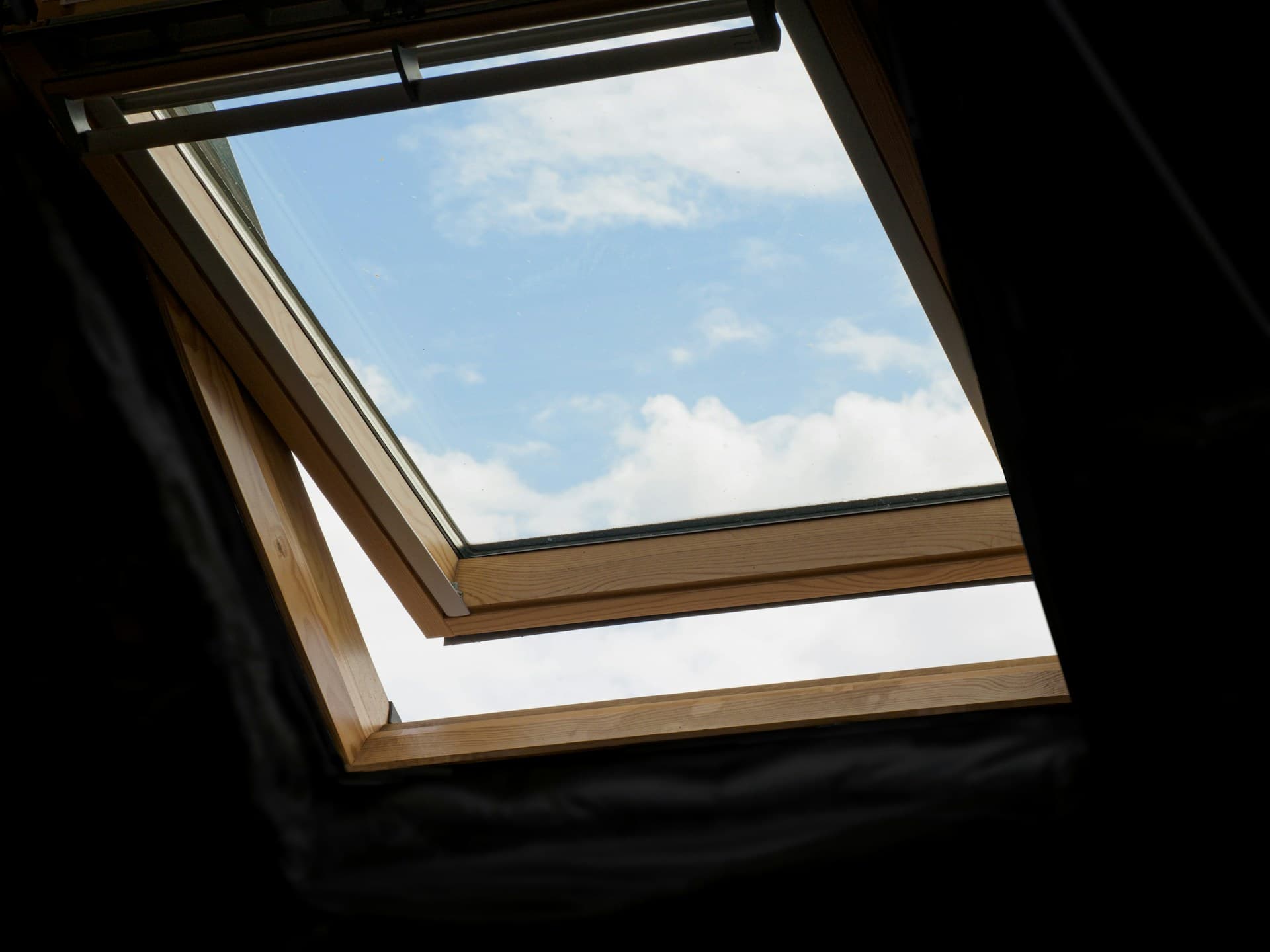 View up through an open timber-framed roof skylight to cloudy blue sky