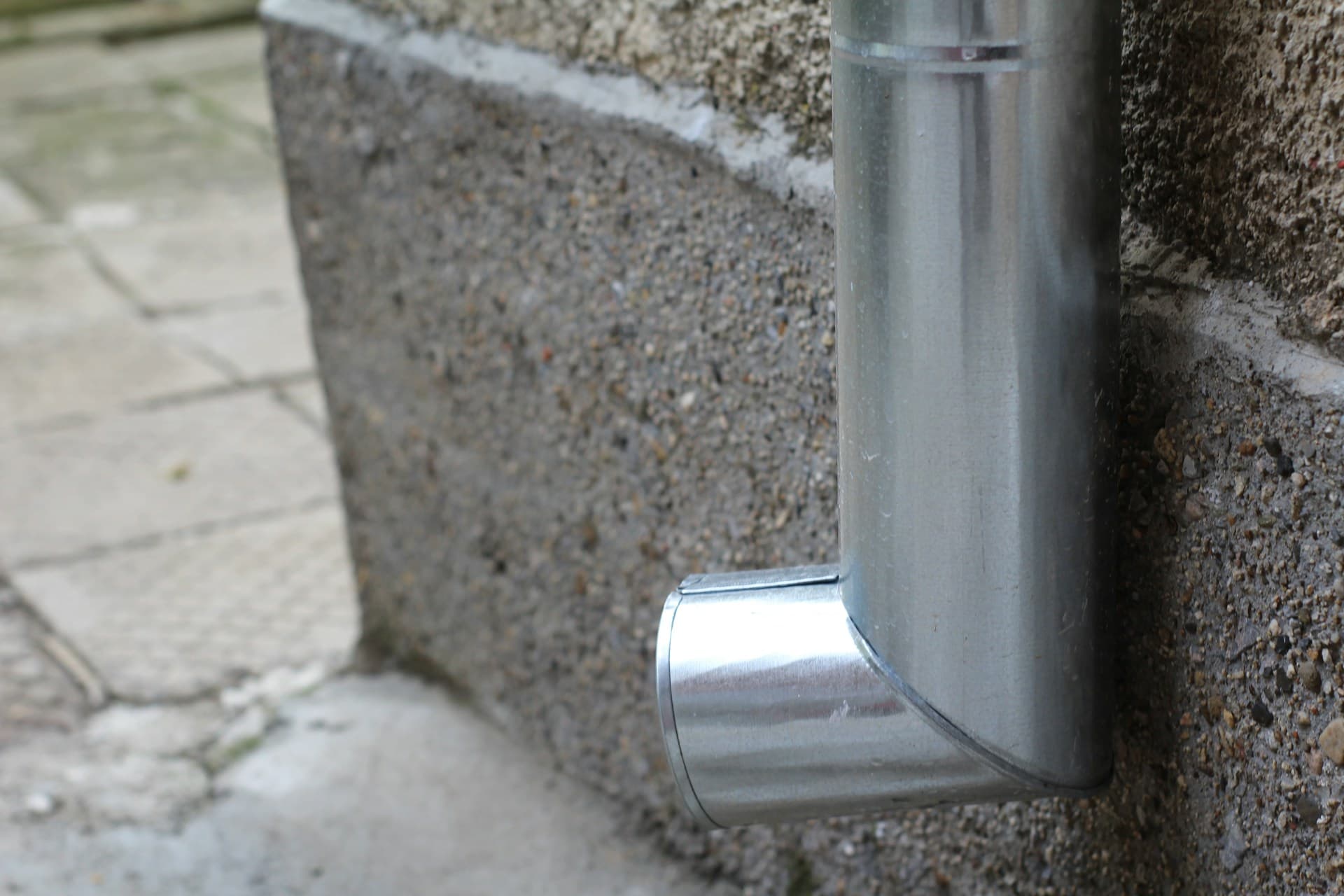 Galvanised metal downpipe with elbow fitting against a concrete block wall
