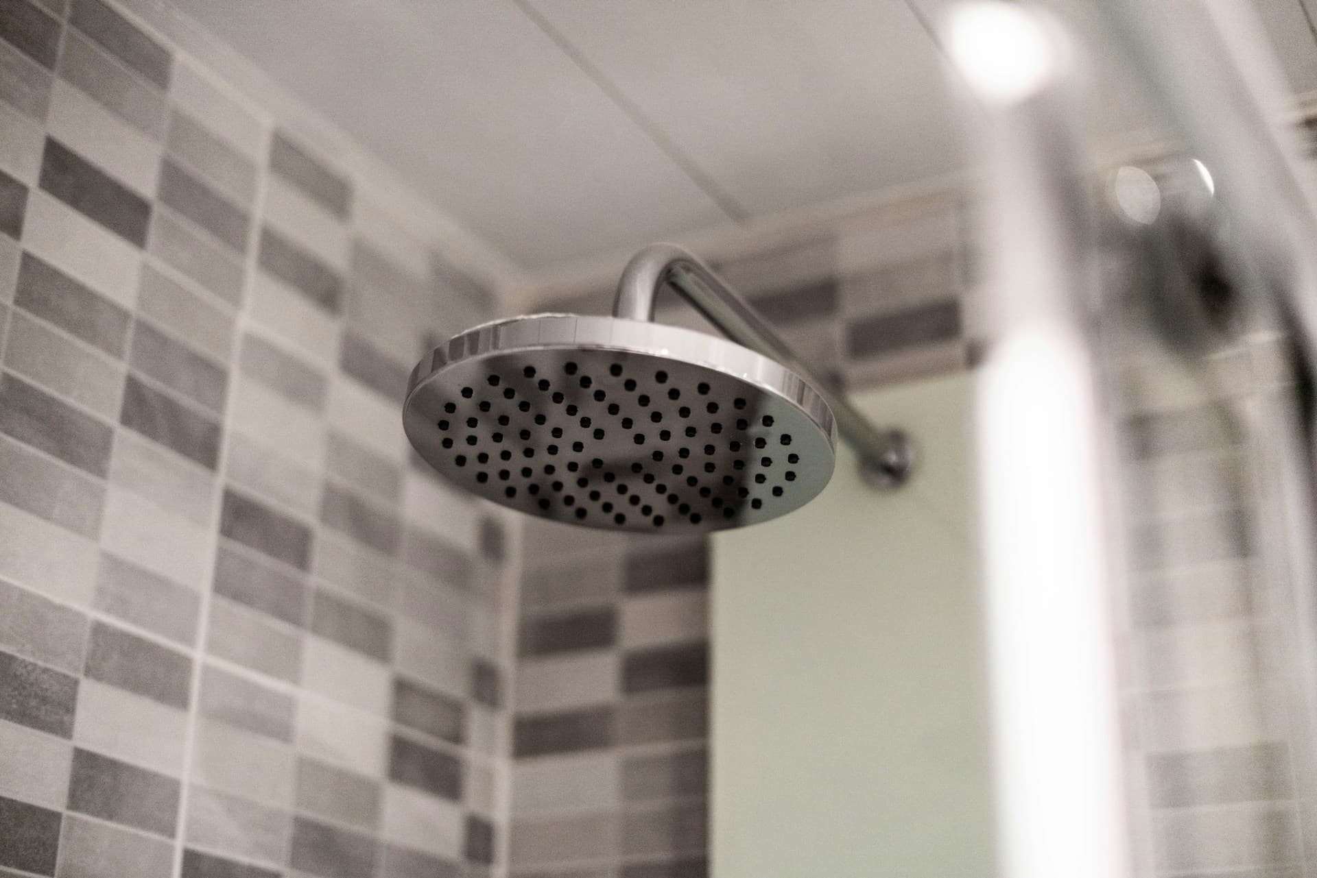 Chrome rainfall showerhead mounted in a grey-tiled shower recess