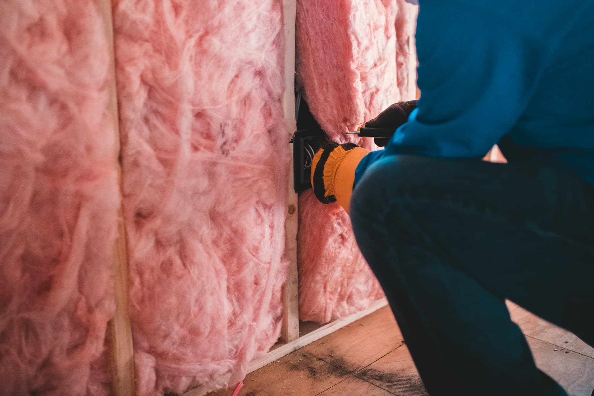 Worker in blue clothing fitting pink batt insulation into a timber-framed wall