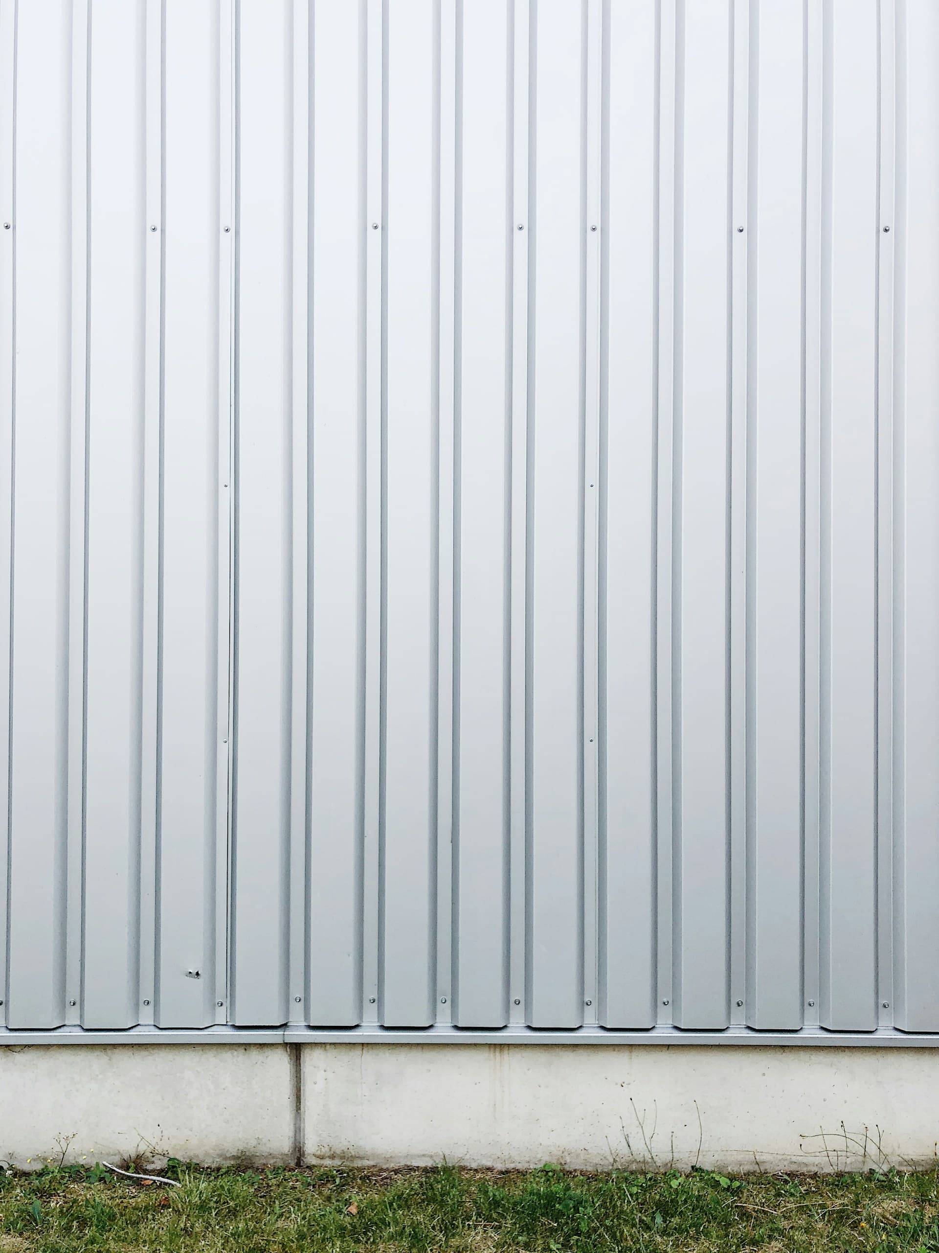 Vertical grey corrugated metal fence on a concrete footing above grass