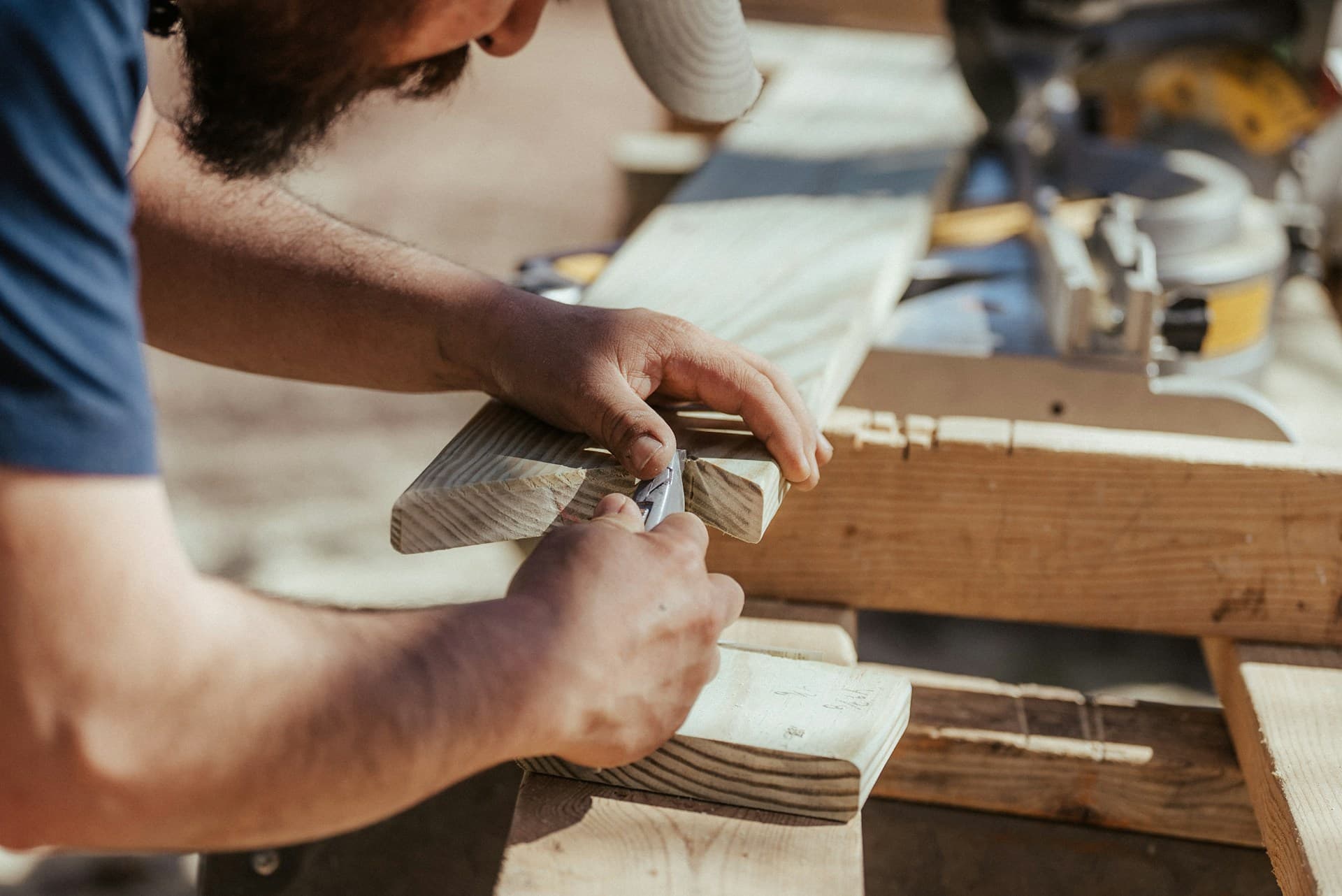 Worker hand-sanding a timber board at an outdoor workbench with power tools