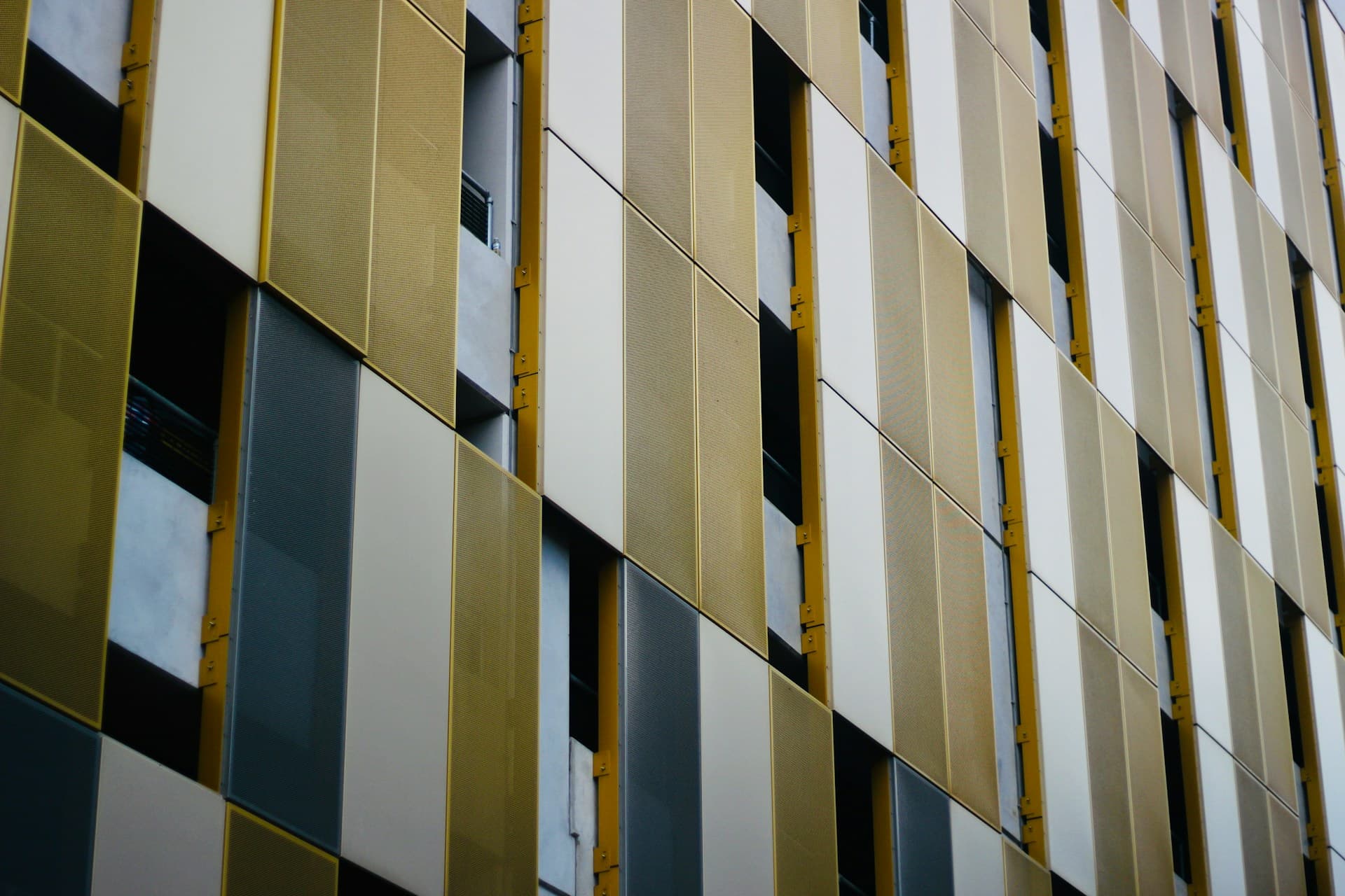 Angled facade of a building clad in gold, grey and white metal panels