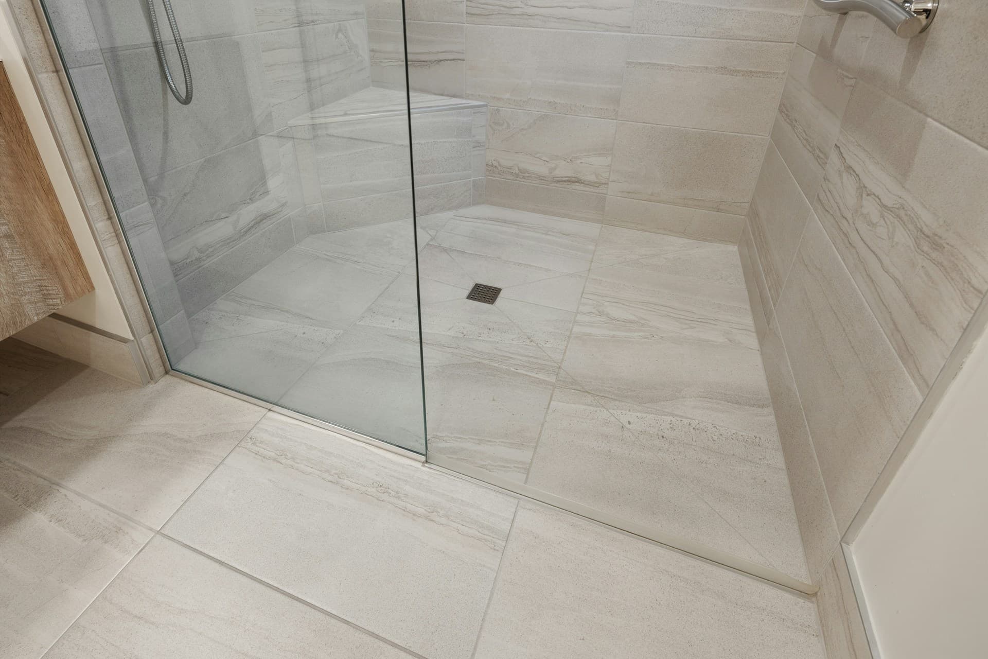 Tiled bathroom floor and walls with a glass shower screen and square drain