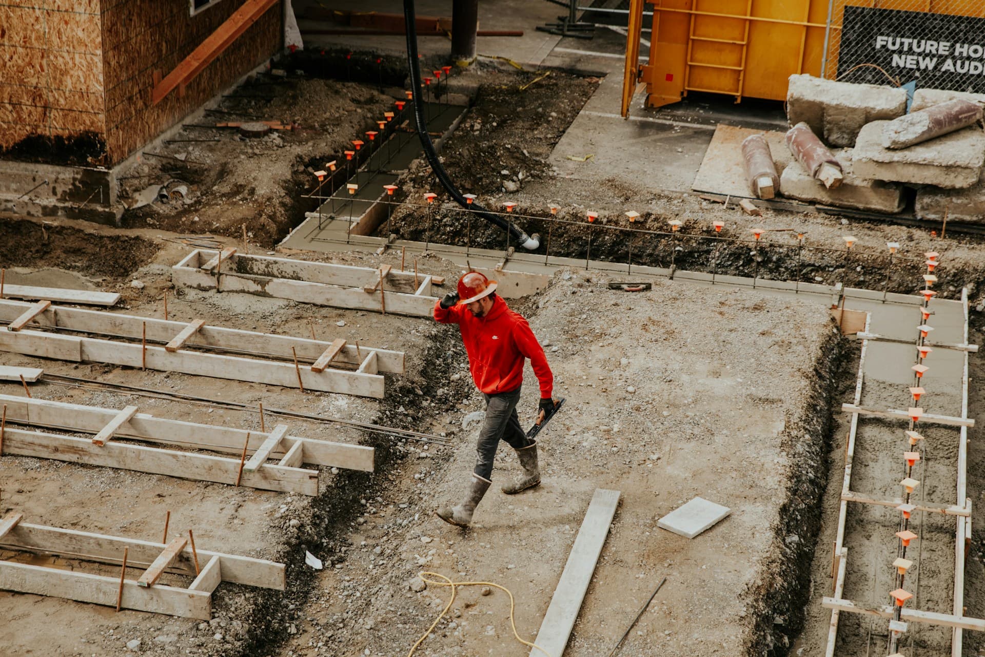 Worker in a red hoodie walking through timber footing formwork on a building site