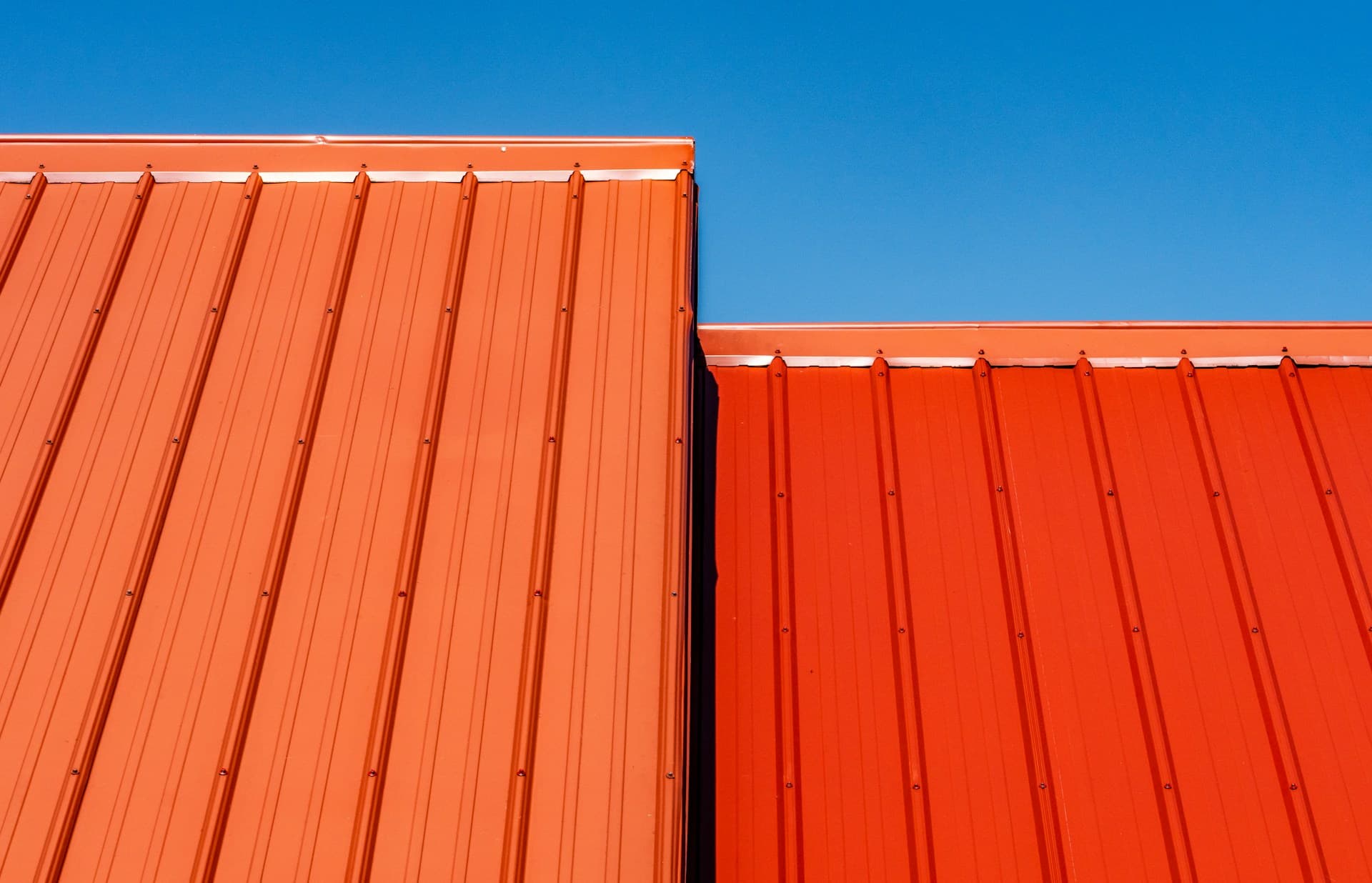 Orange and red corrugated metal roofing panels against a blue sky