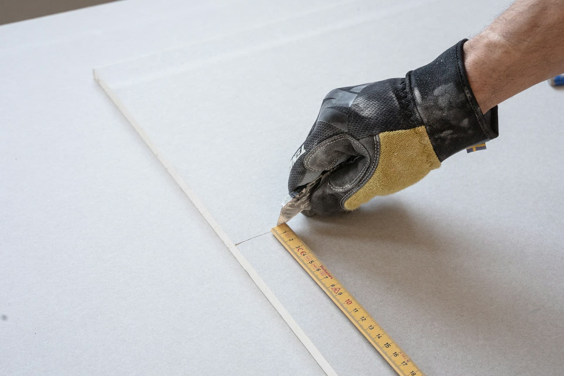Gloved hand marking a plasterboard sheet with a folding wooden rule