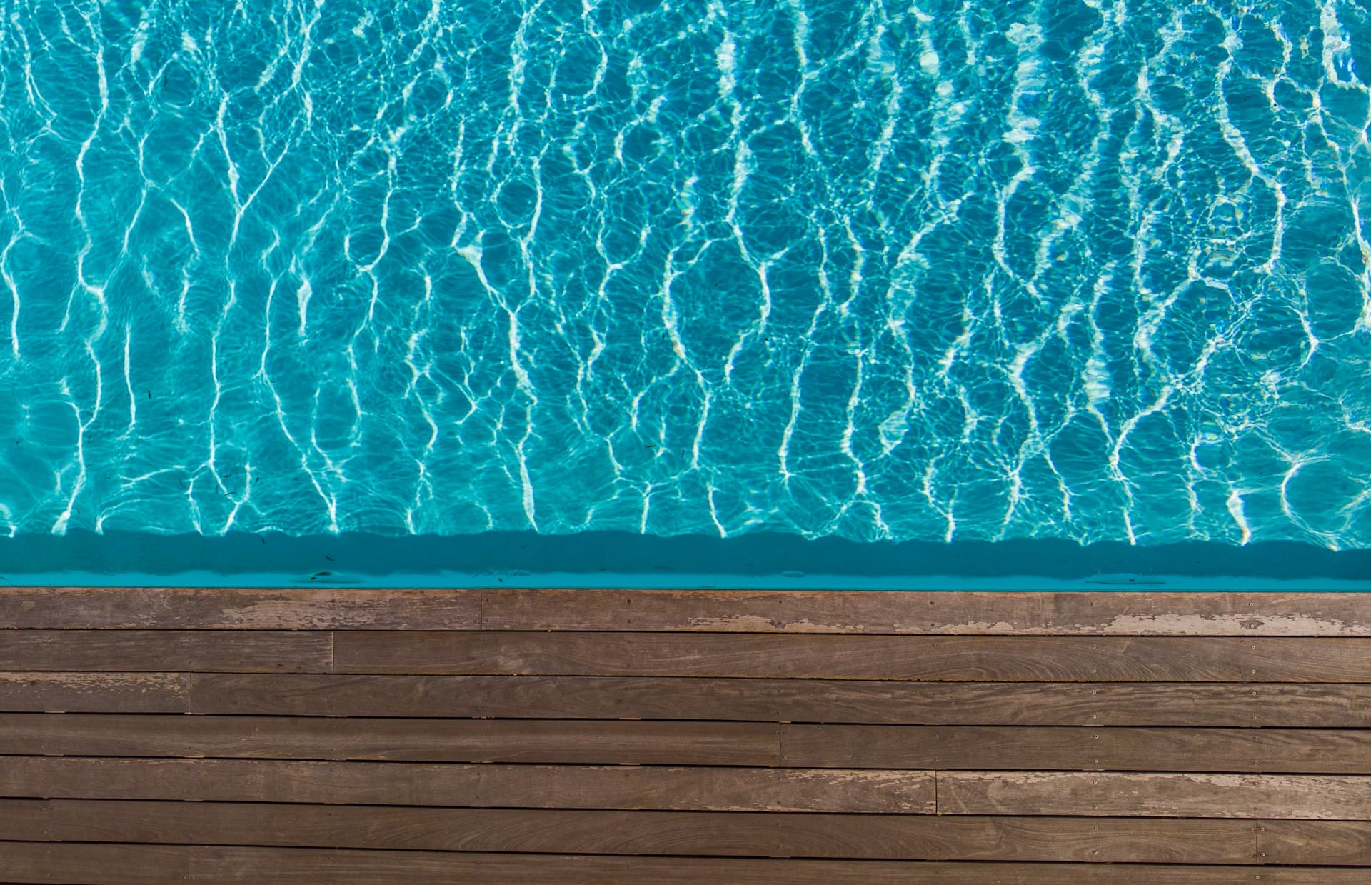 Sunlit turquoise swimming pool water beside a timber decking edge