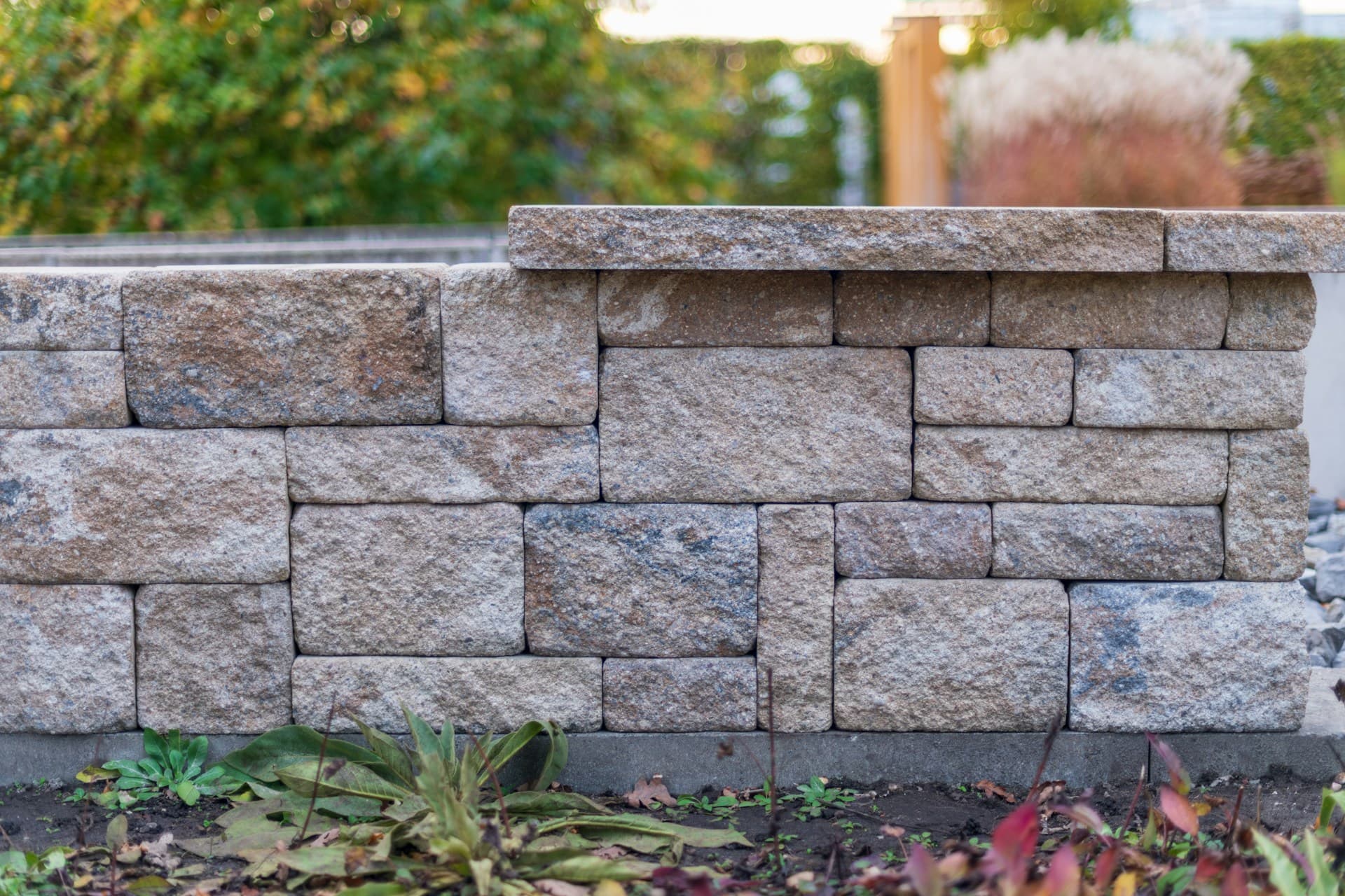 Low stacked-stone garden retaining wall with capping in front of autumn shrubs