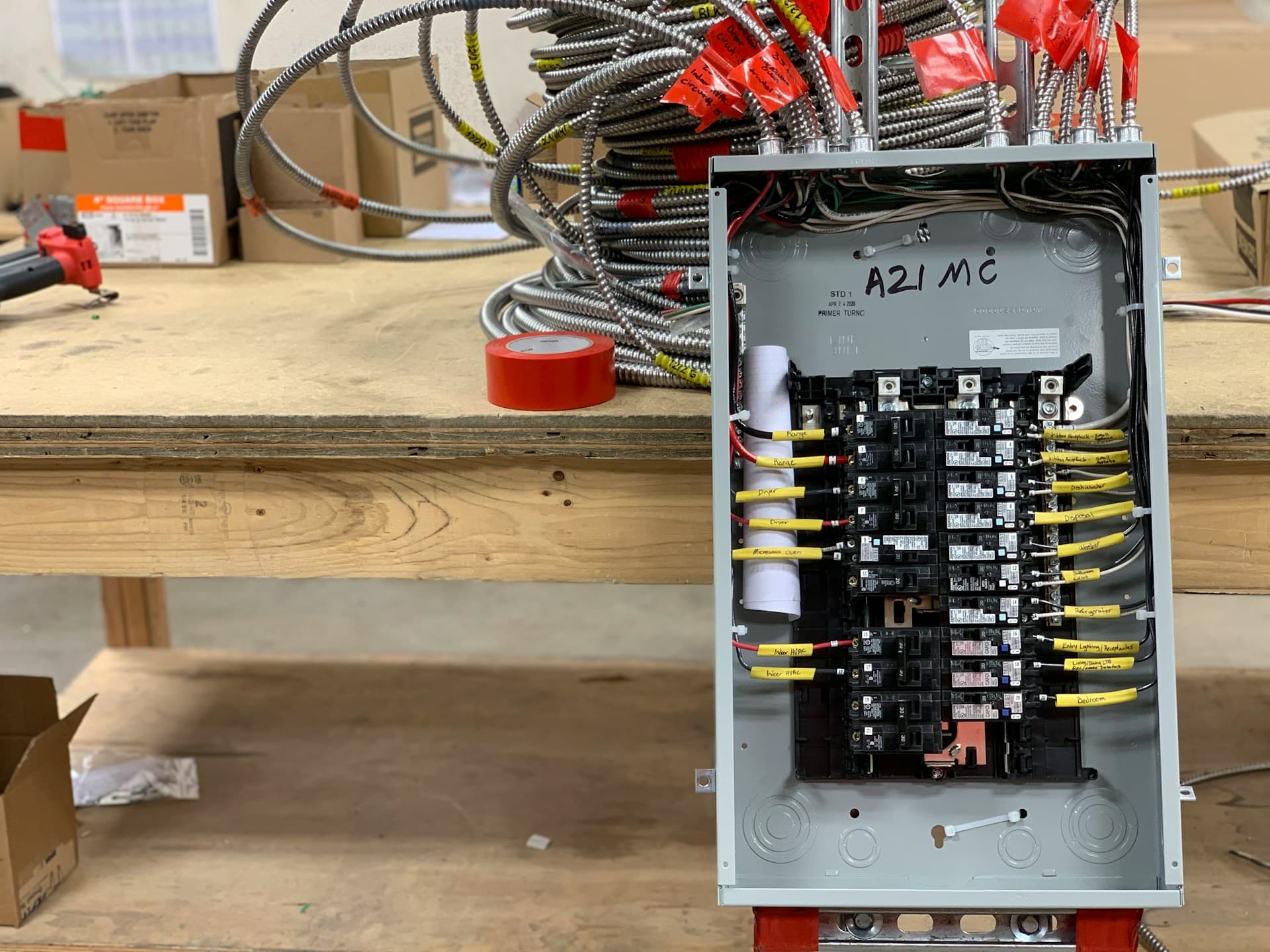 Open electrical switchboard with breakers and looms of wired conduit on a workbench