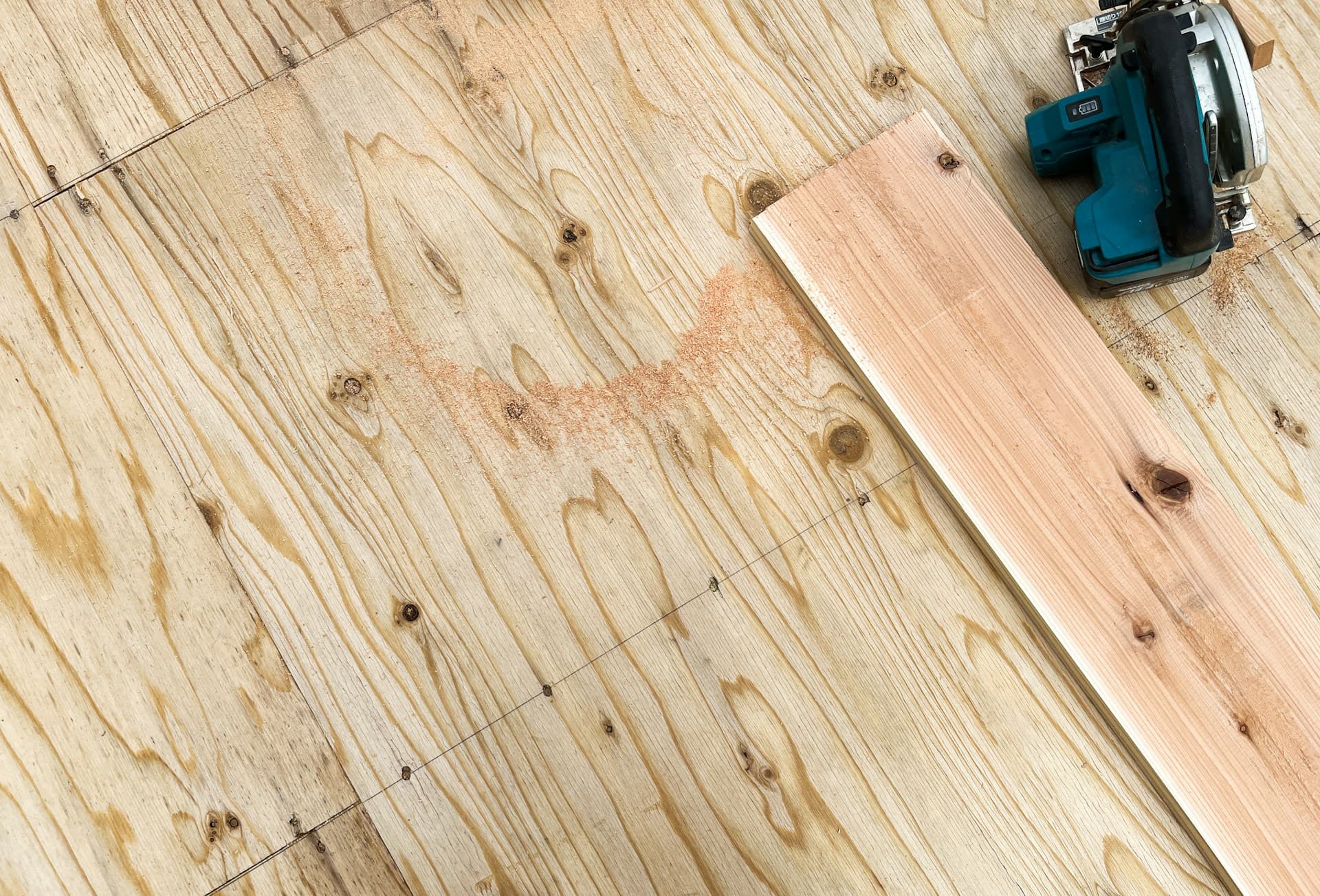 Circular saw cutting a timber board on a plywood subfloor with sawdust